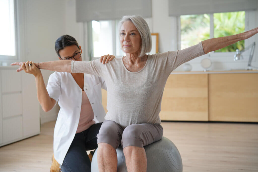 Senior woman exercising with her physiotherapist and swiss ball